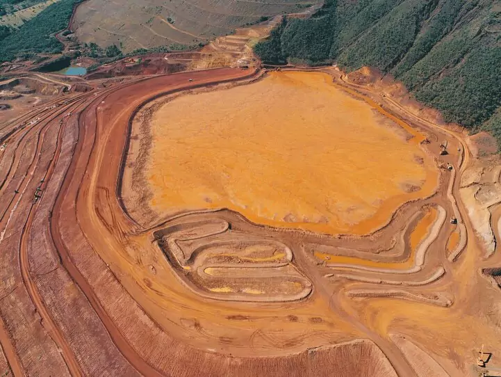 Imagem aérea de uma obra de barragem em construção, mostrando a preparação do terreno com terraplanagem e vias de acesso em torno de uma grande área central.